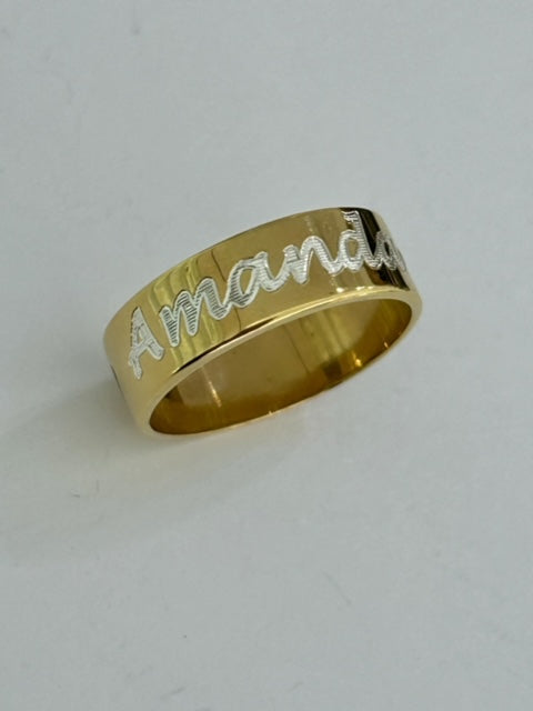A yellow gold ring with the engraved name 'Amanda' on the top surface.