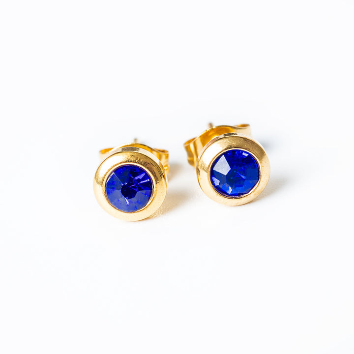 A close up view of the Gabriella Gold Earrings with a blue pendant 
