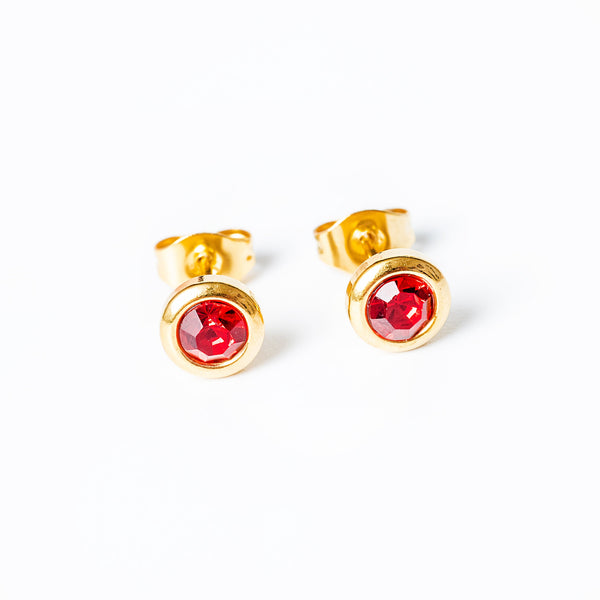 A pair of yellow gold-plated stainless steel earrings with red gemstones set in a classic six-prong setting.