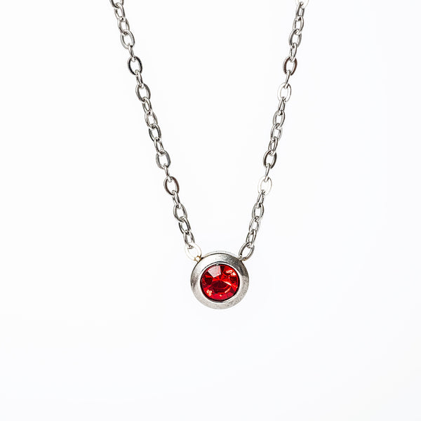 A silver necklace with a red gemstone pendant, displayed against a white background.