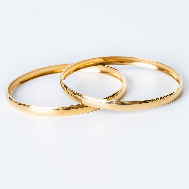 Two gold-colored  Kolina filli stainless steel bracelets with a shiny finish, placed next to each other on a white background.