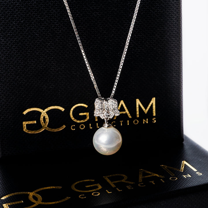 Lena Necklace standing in the center of the image against its uniquely designed box standing behind it. 