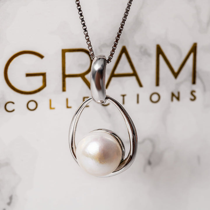 A gram collections's Lola necklace hanging on its chain, in the center of the image, with its box placed behind it. 