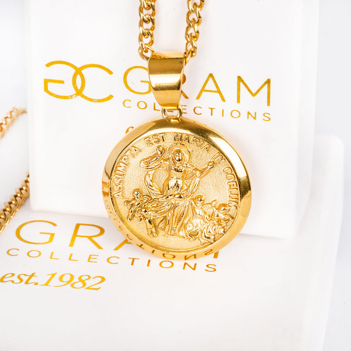 Santa Marija Necklace, attached to the chain, standing in the center of the image in front of its original box.