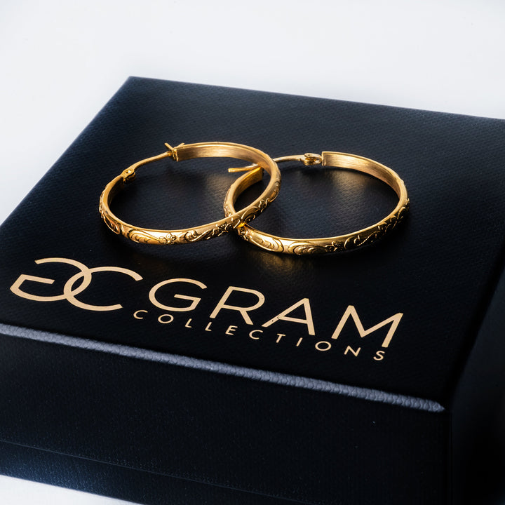 The sue earrings standing on top of each other placed on their box, against a white background. 