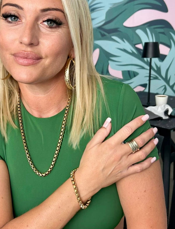A person wearing a green sleeveless top and showcasing a yellow gold stainless steel Tal Pappagal bracelet.