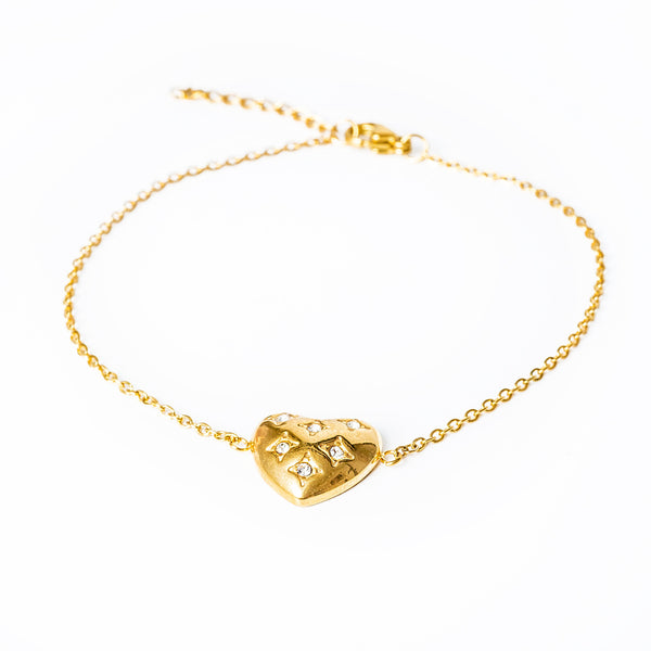 A gold-plated bracelet featuring a heart-shaped charms with cubic zirconia accents, on a white background.