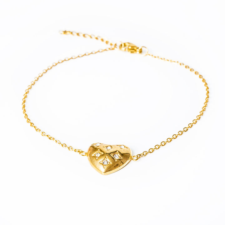 A gold-plated bracelet featuring a heart-shaped charms with cubic zirconia accents, on a white background.