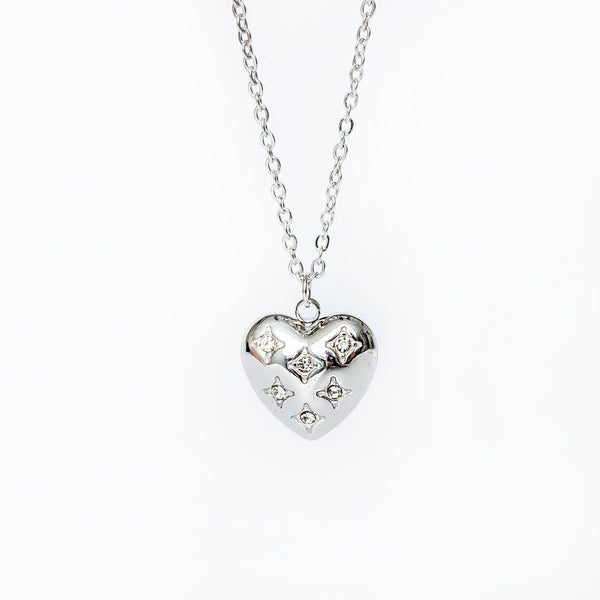 A silver necklace with a heart-shaped pendant adorned with cubic zirconia, displayed against a white background.