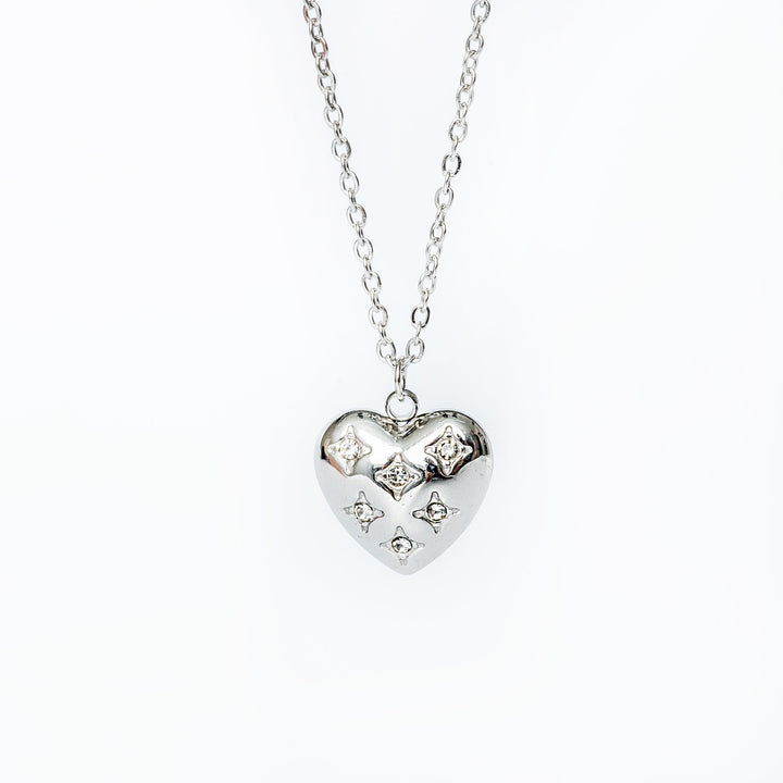 A silver necklace with a heart-shaped pendant adorned with cubic zirconia, displayed against a white background.