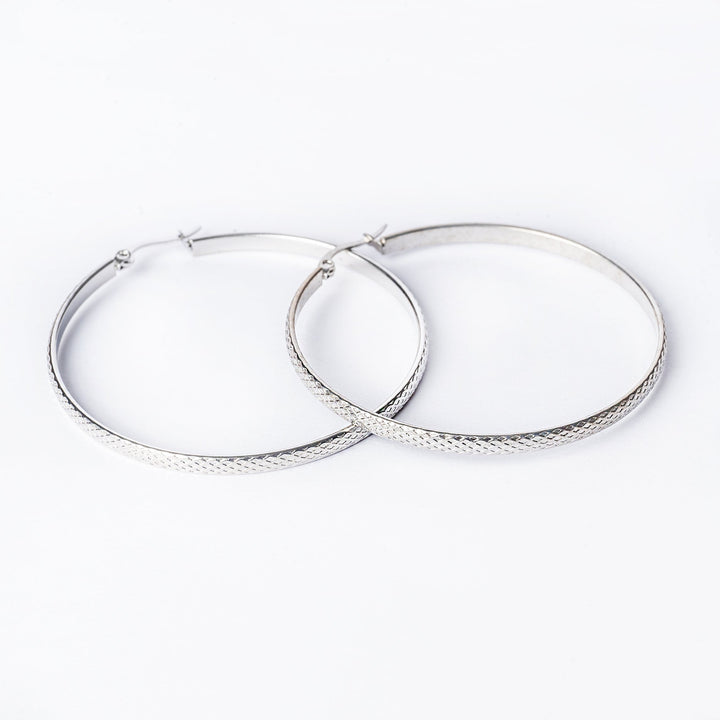 A pair of silver-colored stainless steel hoop earrings with a textured surface, displayed against a white background.