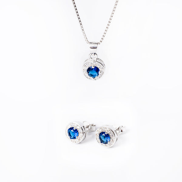 A sterling silver jewelry Baliey  set including a pendant with a blue cubic zirconia, a chain, and a pair of earrings, all displayed against a white background.