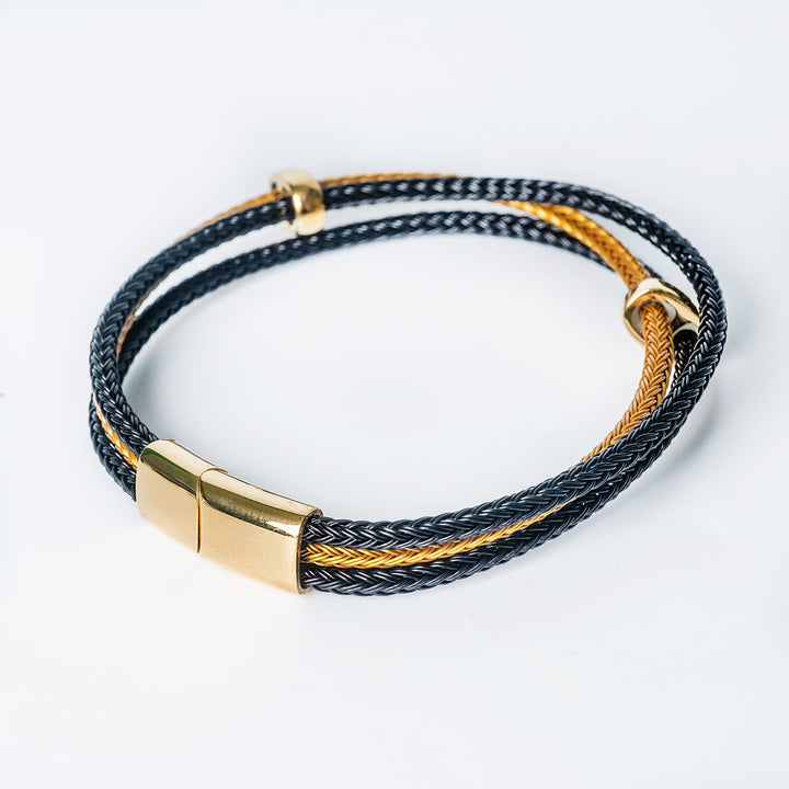 Side view of the Barcelona Bracelet with intertwined black and gold braids and a polished gold clasp