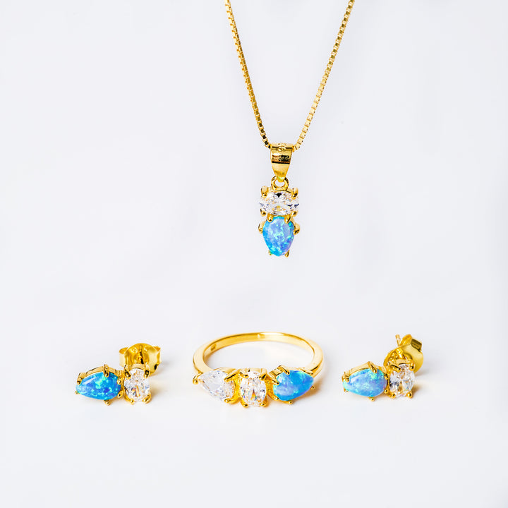 A set of rose gold-colored jewelry including a ring, a necklace, and two earrings, each featuring a central blue cubic zirconia gemstone.