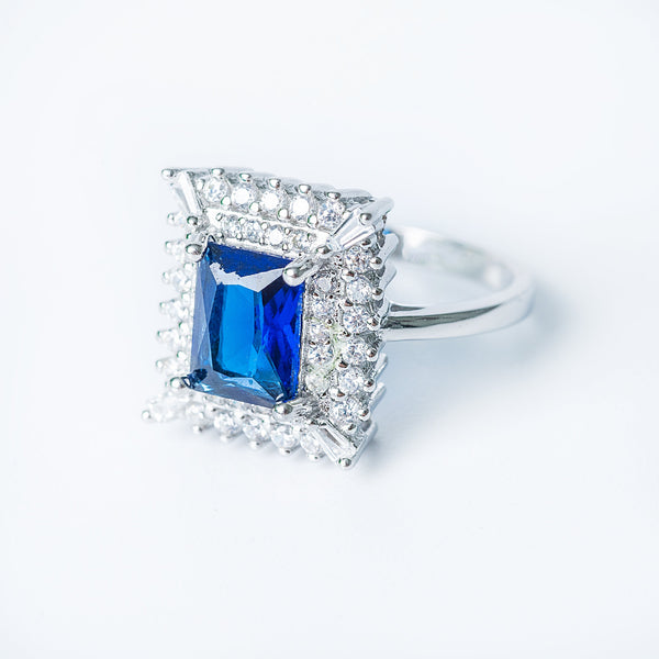 A sterling silver Diana ring featuring a large blue colored cubic zirconia gemstone surrounded by smaller clear cubic zirconia accents, set in a classic six-prong setting.