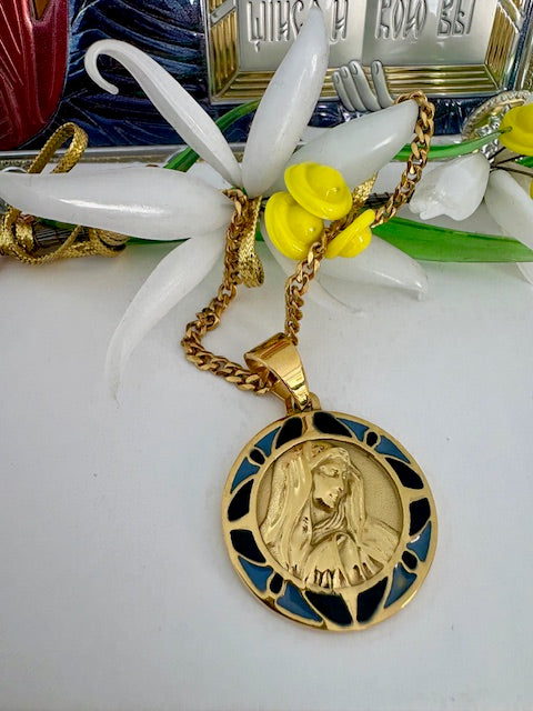 A stainless steel Duluri necklace with a yellow gold plating featuring a round pendant, displayed with a white flower and yellow fruit in the background.