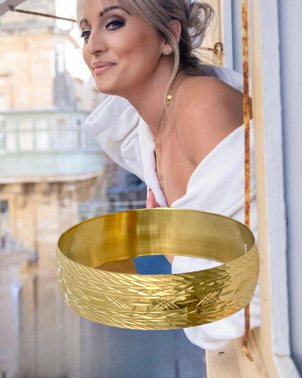 A woman wearing a white off-shoulder top, showcasing a yellow gold, textured Wiesgha Maltese bracelet on her wrist.
