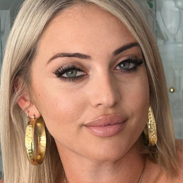 A person wearing yellow gold fili earrings with a textured Maltese style design, displayed prominently in the image.