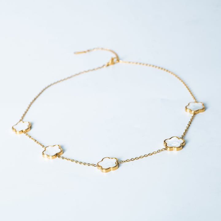 Gold Fiore necklace featuring white mother-of-pearl flower-shaped links shown from a side angle on a white background