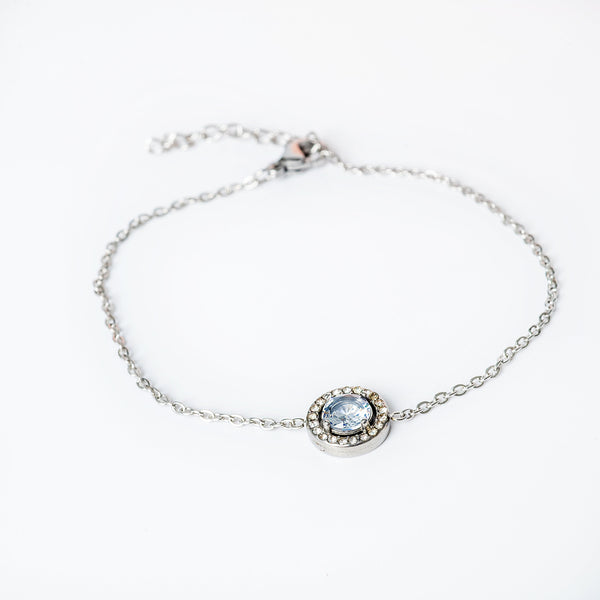 A silver bracelet with a central blue cubic zirconia gemstone, surrounded by smaller clear crystals, all attached to a silver chain.