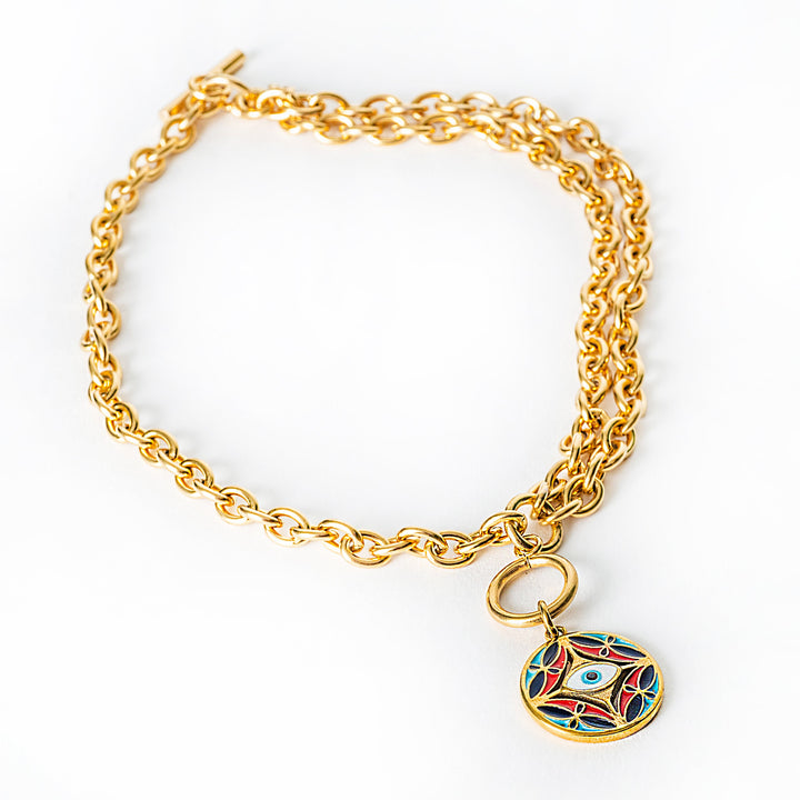 A close up view of gold chain Ghajn bracelet with a colorful pendant on a white background