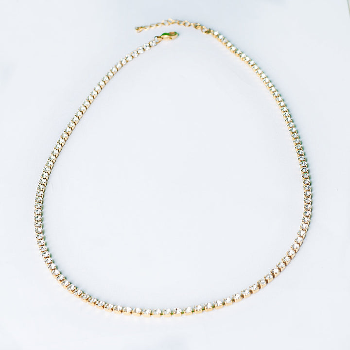 Gold tennis necklace with a full row of clear stones shown in a front view