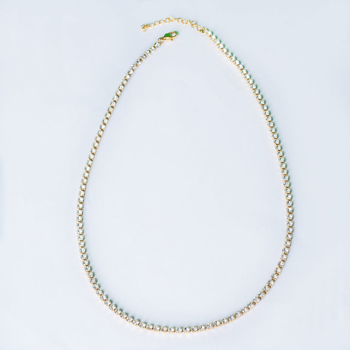 Gold tennis necklace with clear stones shown in a top-down view