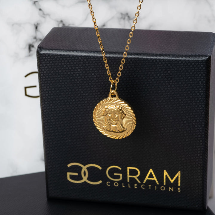 Gold Saviour necklace with a pendant on a black box labeled '3C Gram Collections'.