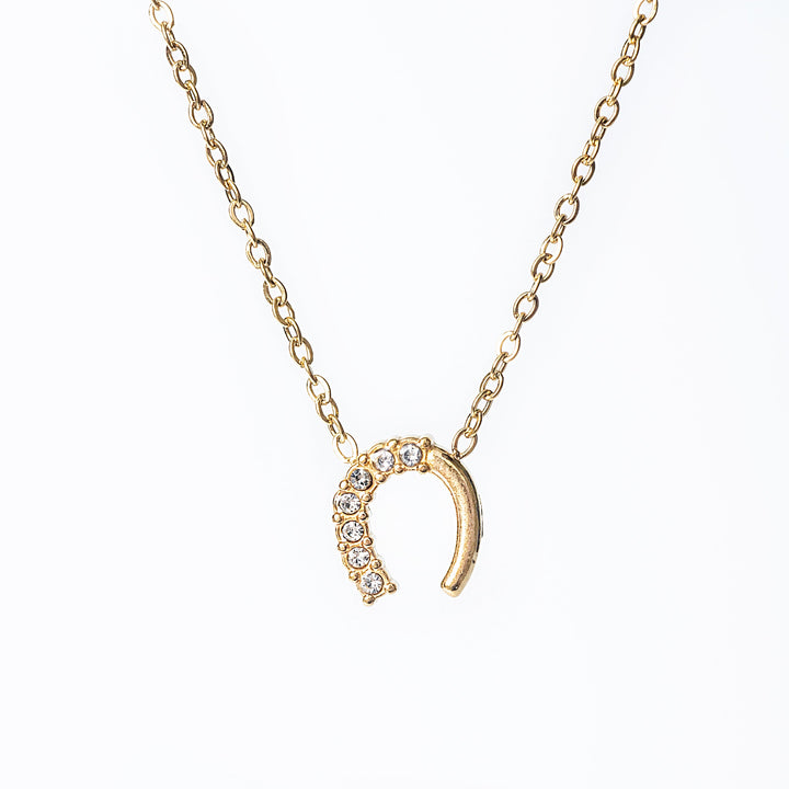 Gold horseshoe necklace with crystal detailing hanging from a fine gold chain