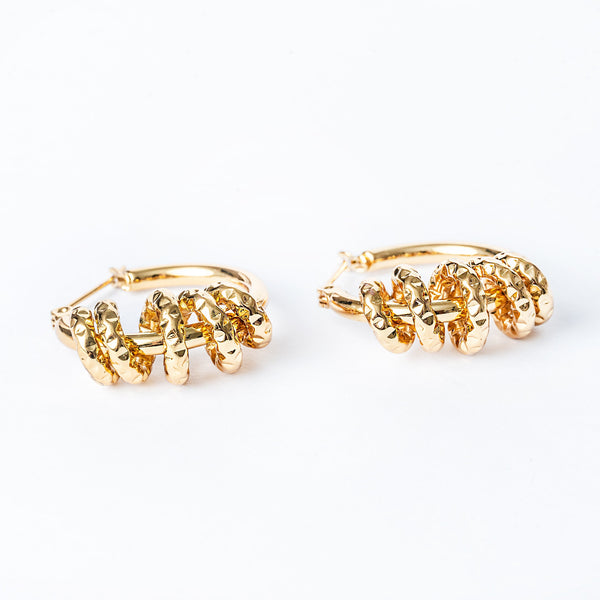 A pair of yellow gold-colored hoop Karen earrings with a textured surface on a white background.