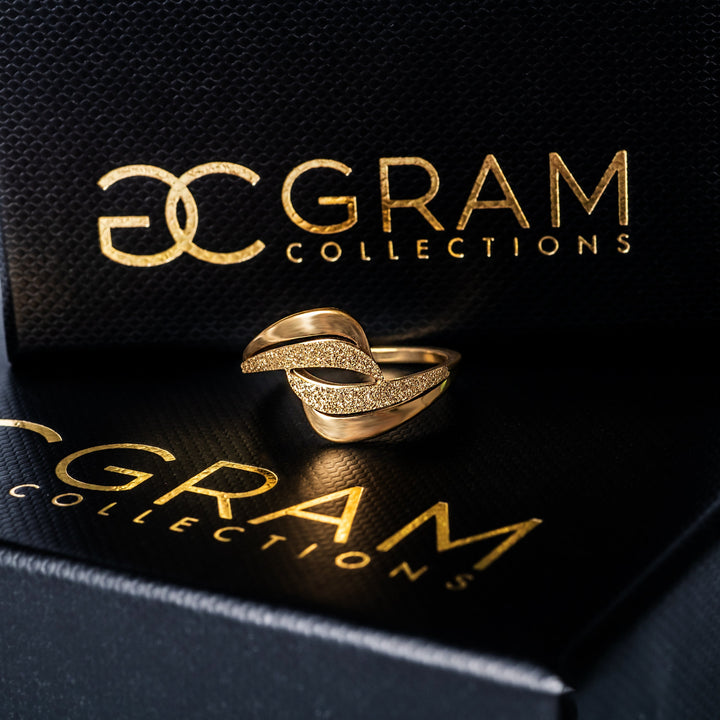 Gram collections'sKaycee Gold Ring standing in the center of the image placed on its uniquely designed box. 