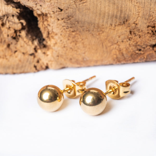 A pair of gold-plated stainless steel stud earrings displayed against a wooden textured background.