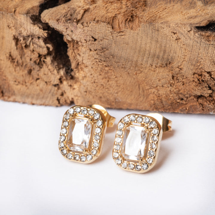 A pair of gold-plated stainless steel earrings with AAA cubic zerconia gems, displayed on a wooden surface.