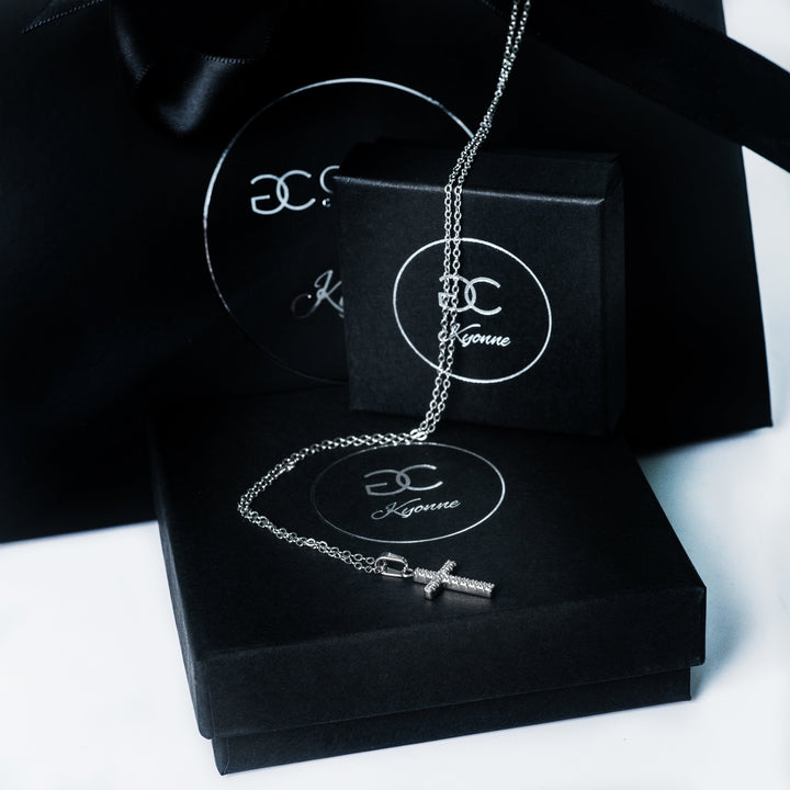 Silver Kyonne cross necklace with a diamond covered pendant displayed on black branded packaging