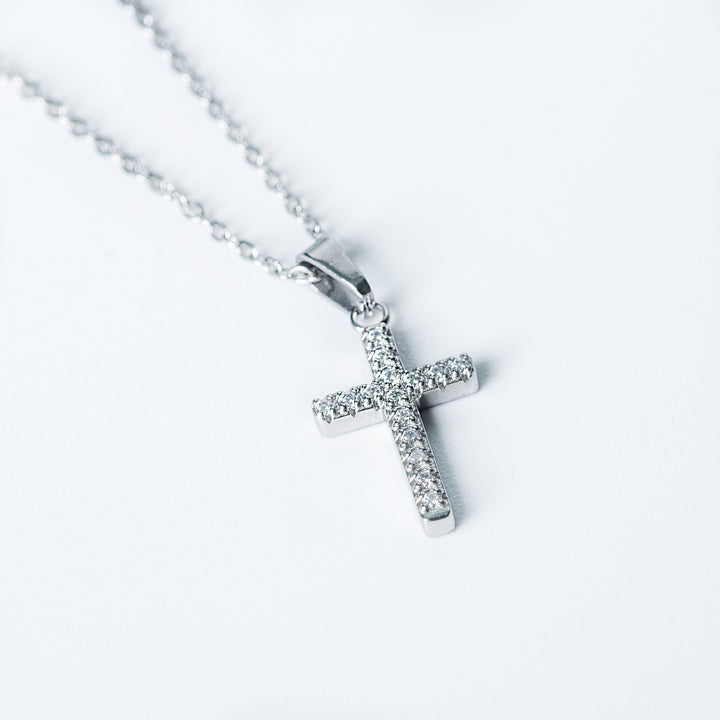 Macro close up of the silver Kyonne cross necklace with clear diamonds on a white background