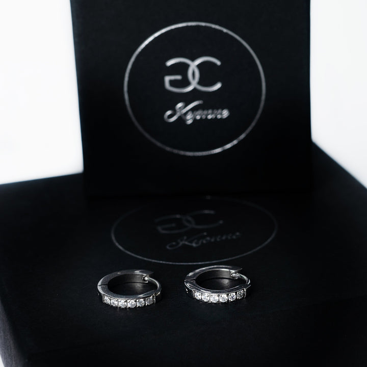 Silver Kyonne hoop earrings with a row of clear diamonds displayed on a black branded box