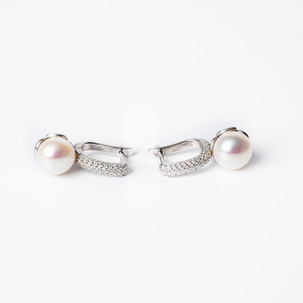 A pair of silver  Layla earrings featuring a pearl embellishment on each, set against a white background.