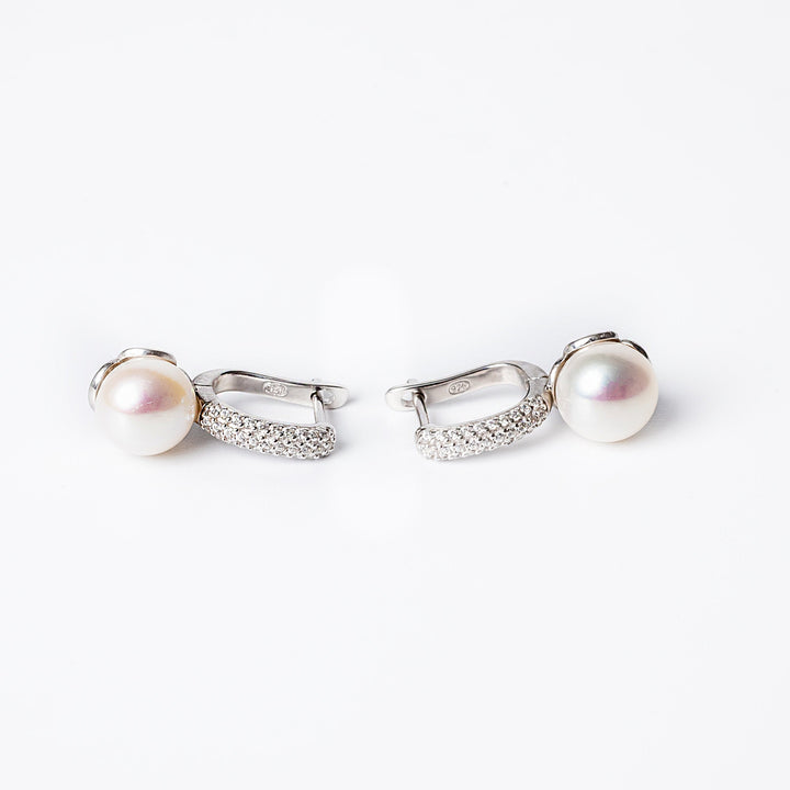 A pair of silver  Layla earrings featuring a pearl embellishment on each, set against a white background.