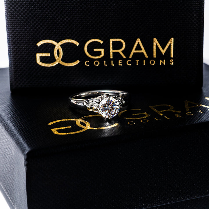 A silver Louise ring standing in the center of the image, placed on its uniquely designed box. 