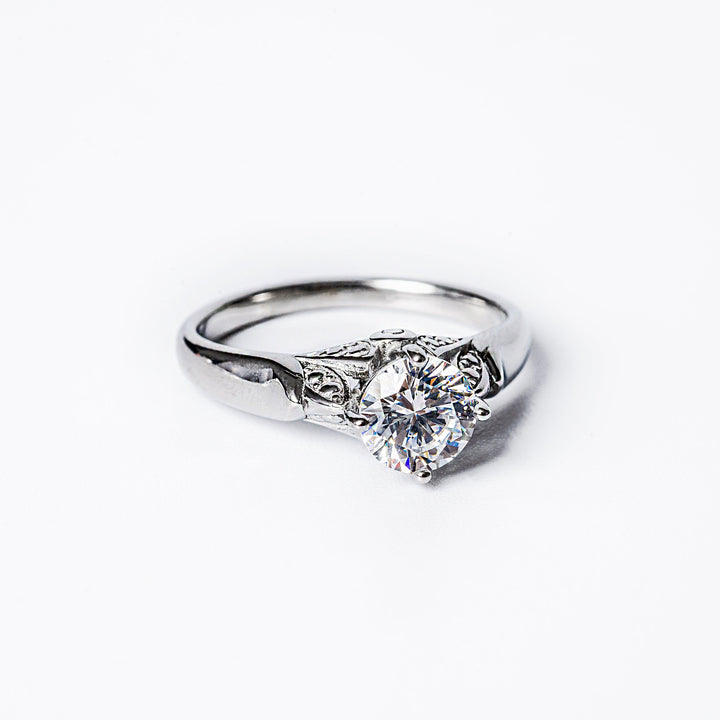 A silver ring featuring a prominent cubic zirconia gemstone in a classic six-prong setting, surrounded by a textured band.