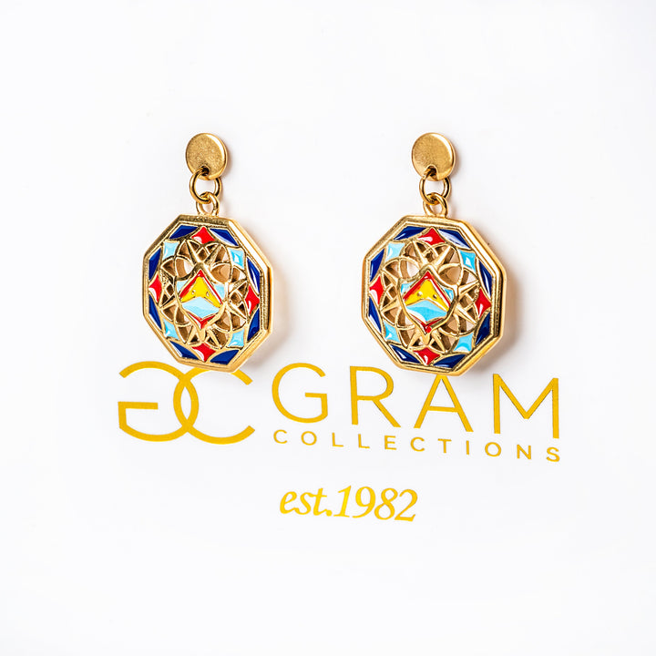 A close up view of Luzzu earrings standing in the center of the image attached to its uniquely designed box. 