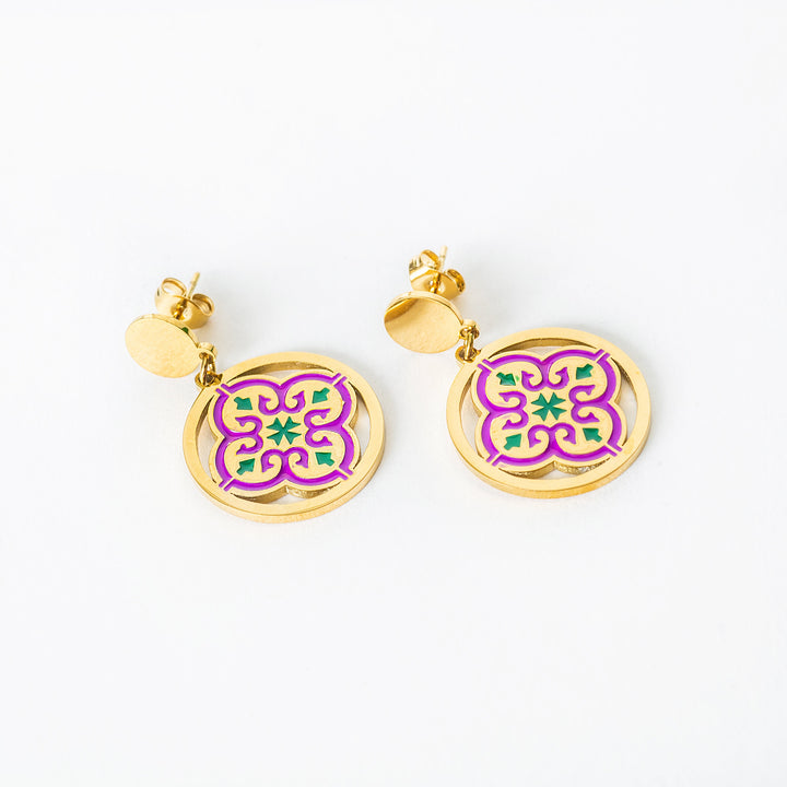 A close up viee of Maduma  earrings with purple and green designs on a white background