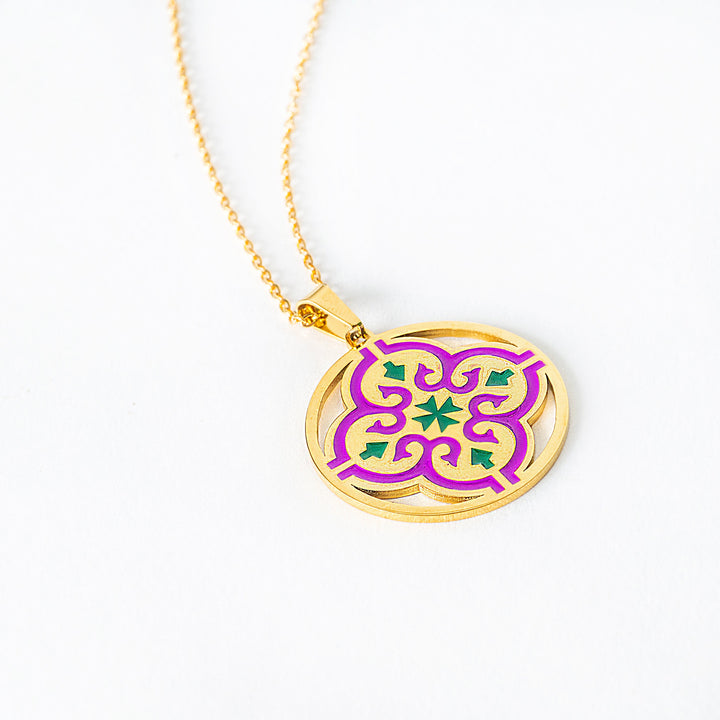 A lose up view of Maduma necklace with a purple and green pendant on a white background