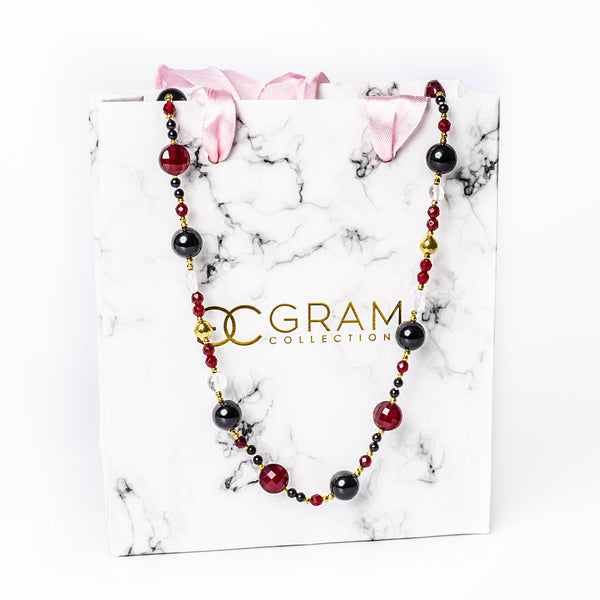 A maroon necklace placed on its box, standing in the center of the image against a white background. 