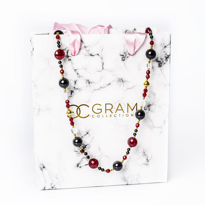 A maroon necklace placed on its box, standing in the center of the image against a white background. 