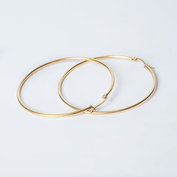 Gold Maya hoop earrings crossed on a white background