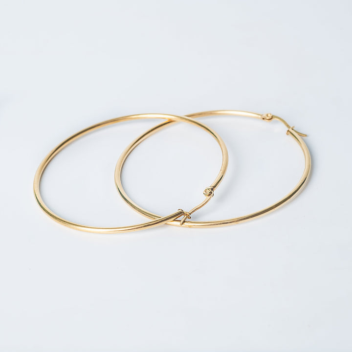 Gold Maya hoop earrings crossed on a white background