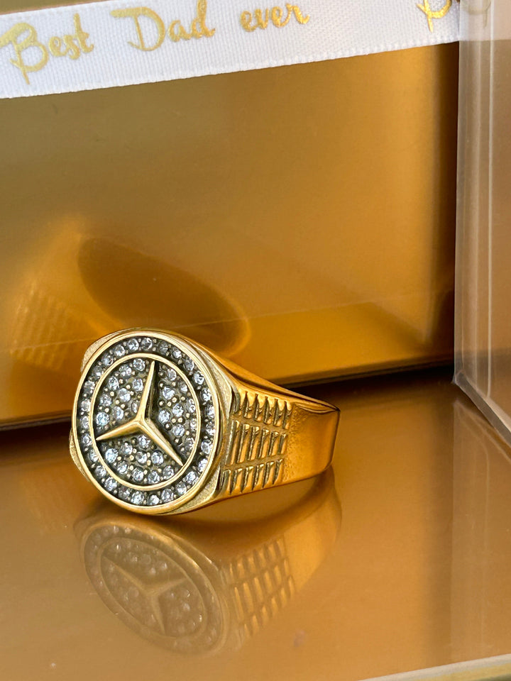A left side view of Mercedes Ring standing in the right angle of the image, placed on golden surface. 