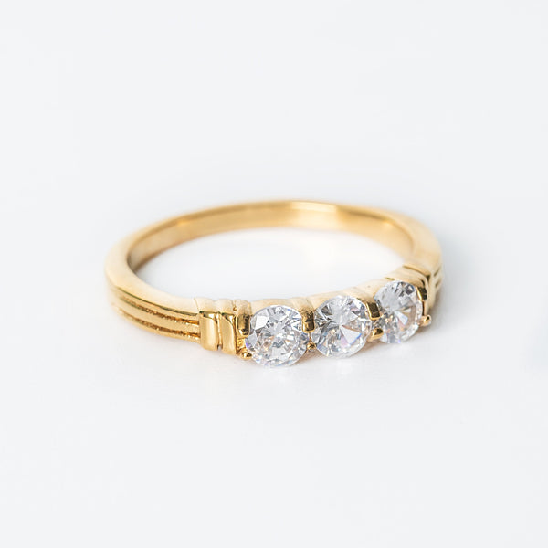 Close-up view of gold Mia ring featuring three round clear gemstones in a polished band.