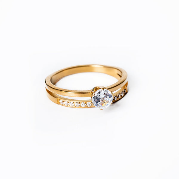 A gold-plated stainless steel ring with a yellow gold finish, featuring a central cubic zirconia gemstone, surrounded by smaller clear crystals.